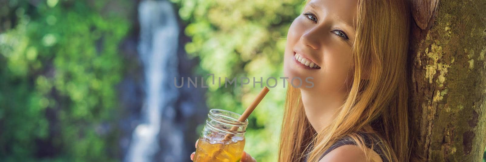 Closeup portrait image of a beautiful woman drinking ice tea with feeling happy in green nature and waterfall garden background BANNER, LONG FORMAT by galitskaya