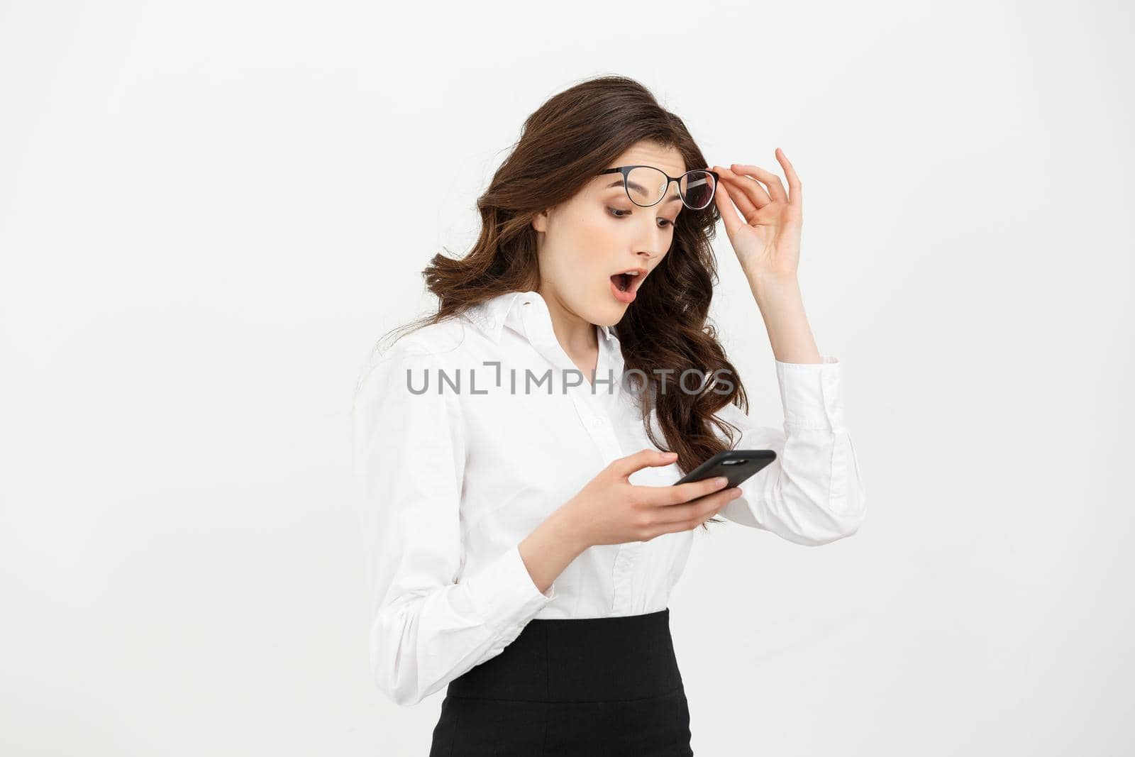 Business Concept: Surprised youngwoman holding mobile phone and staring at it while standing against grey background.