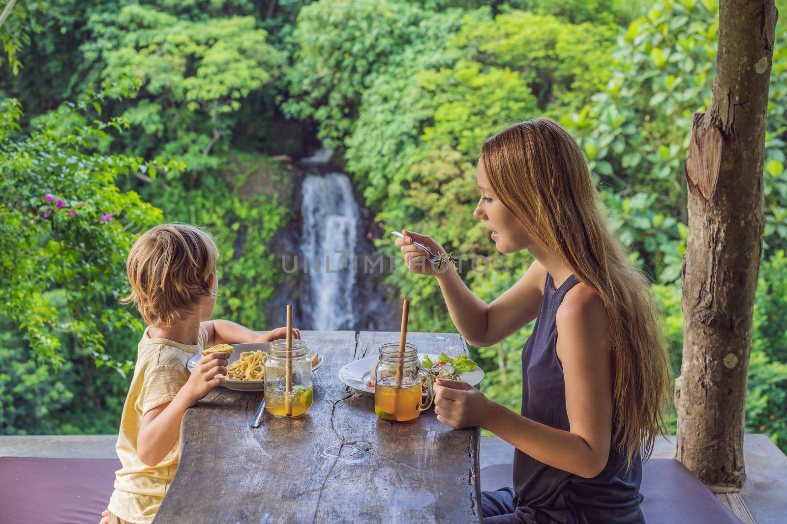 Mom and son tourists in a cafe on the background of a waterfall. Traveling with kids concept. What to do with children. Child friendly place by galitskaya