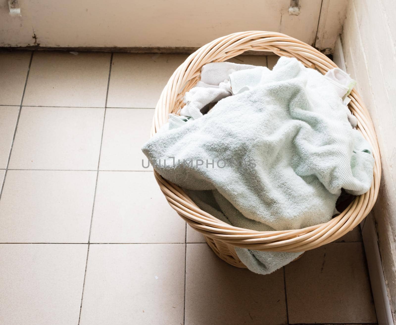 High angle view of towels in wicker laundry basket on rustic tiled floor (selective focus)