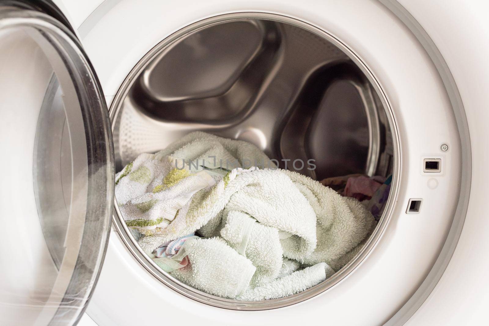 Close up of wet towels in front loading washing machine (selective focus) by natalie_board