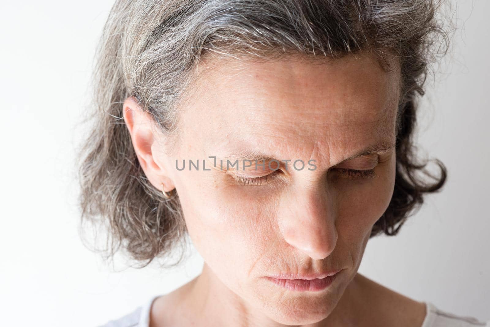 Close up of distressed middle aged woman with grey hair looking down (selective focus)