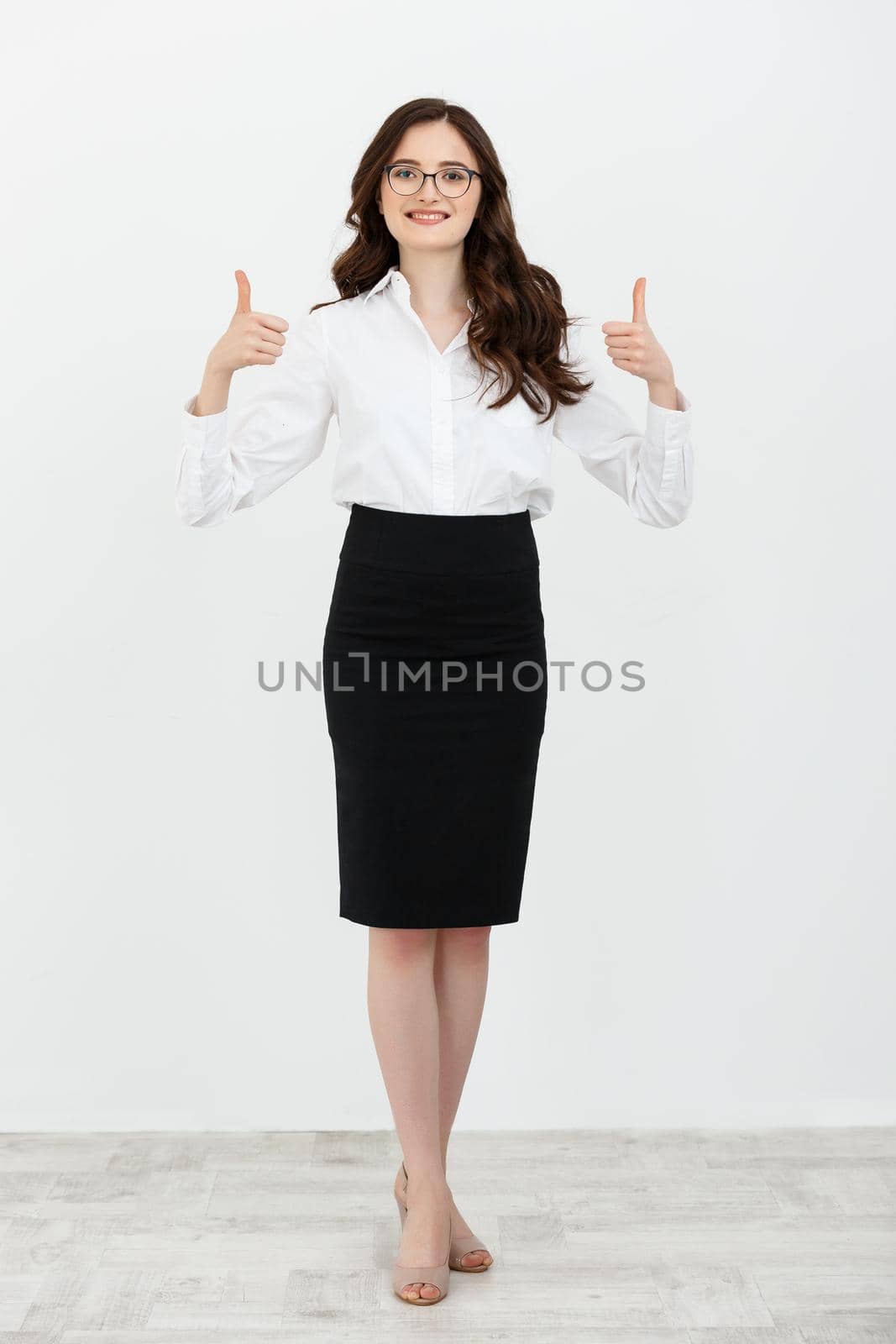 Full length portrait of a beautiful woman in a suit giving a thumb up isolated over white studio background