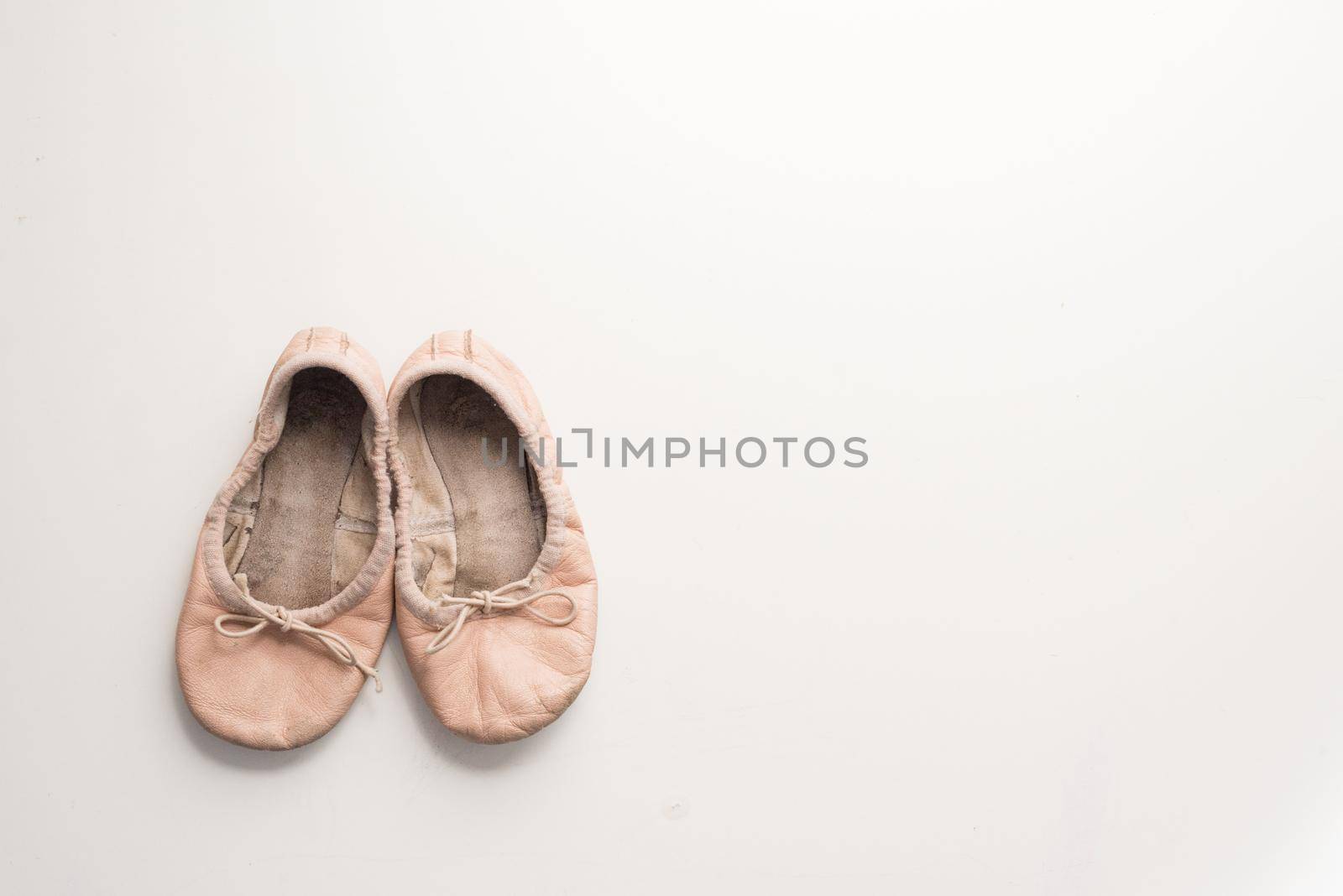High angle view of old, dirty little girl's pink ballet shoes on white table with copy space to right