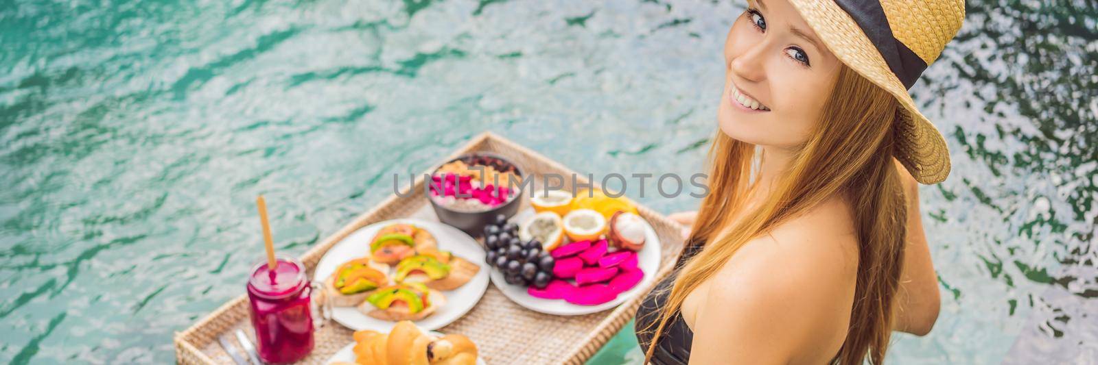 BANNER, LONG FORMAT Breakfast tray in swimming pool, floating breakfast in luxury hotel. Girl relaxing in the pool drinking smoothies and eating fruit plate, smoothie bowl by the hotel pool. Exotic summer diet. Tropical beach lifestyle. Bali Trend by galitskaya