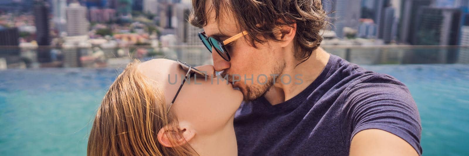 BANNER, LONG FORMAT young happy and attractive playful couple taking selfie picture together at luxury urban hotel infinity pool and panoramic view of the city enjoying holidays honeymoon travel in diversity ethnicity and love by galitskaya