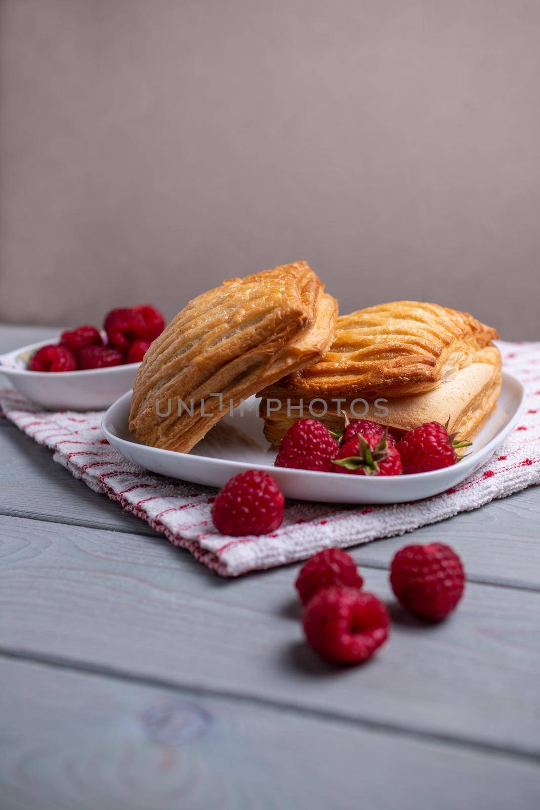 Delicious fresh pastries with raspberries in a white plate on a wooden table. by bySergPo