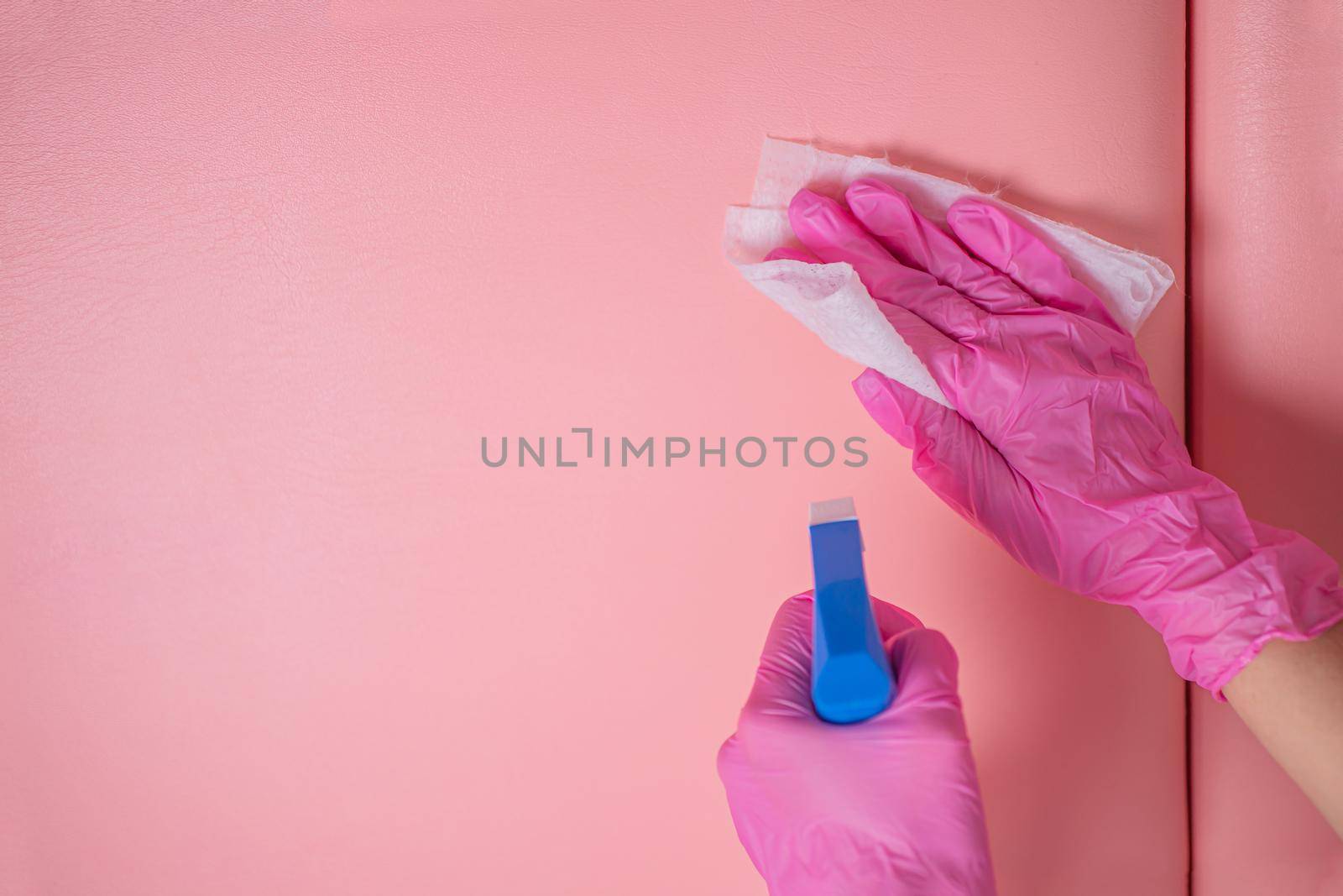 An employee in pink gloves disinfects the patient's couch with a disinfectant spray and a clean napkin. The staff cleans to prevent the spread of viruses and bacteria.