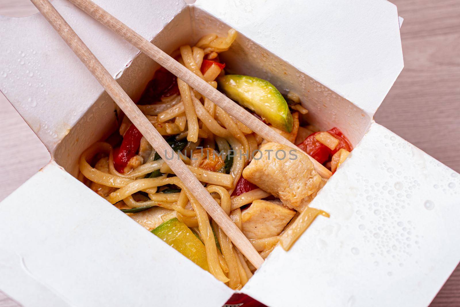 chinese food egg noodles with chicken and vegetables close-up. Open paper box