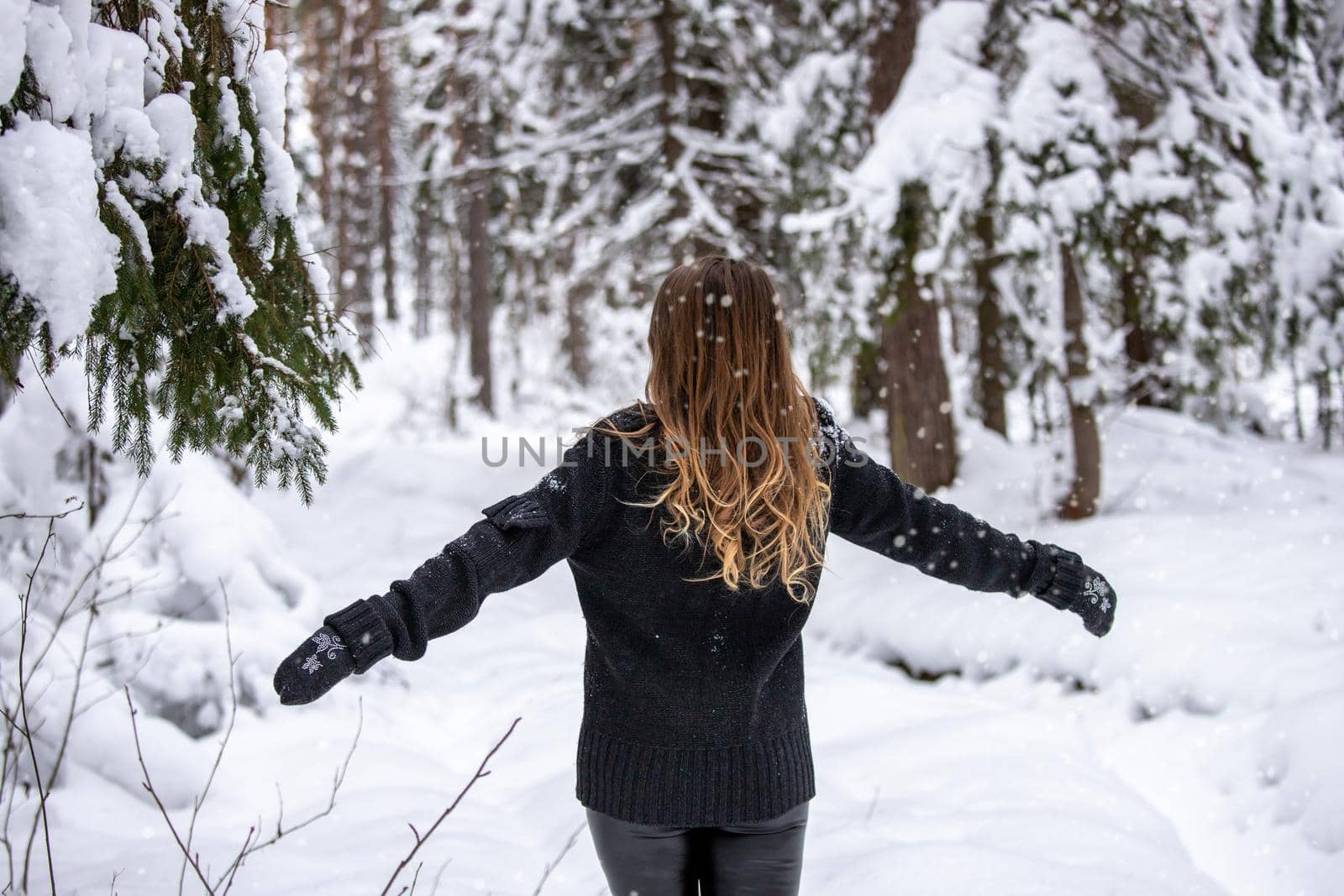 Young adult woman alone slowly walking on snow covered boardwalk after snowfall. Enjoying fresh air in park. Peaceful atmosphere in winter day. Back view.