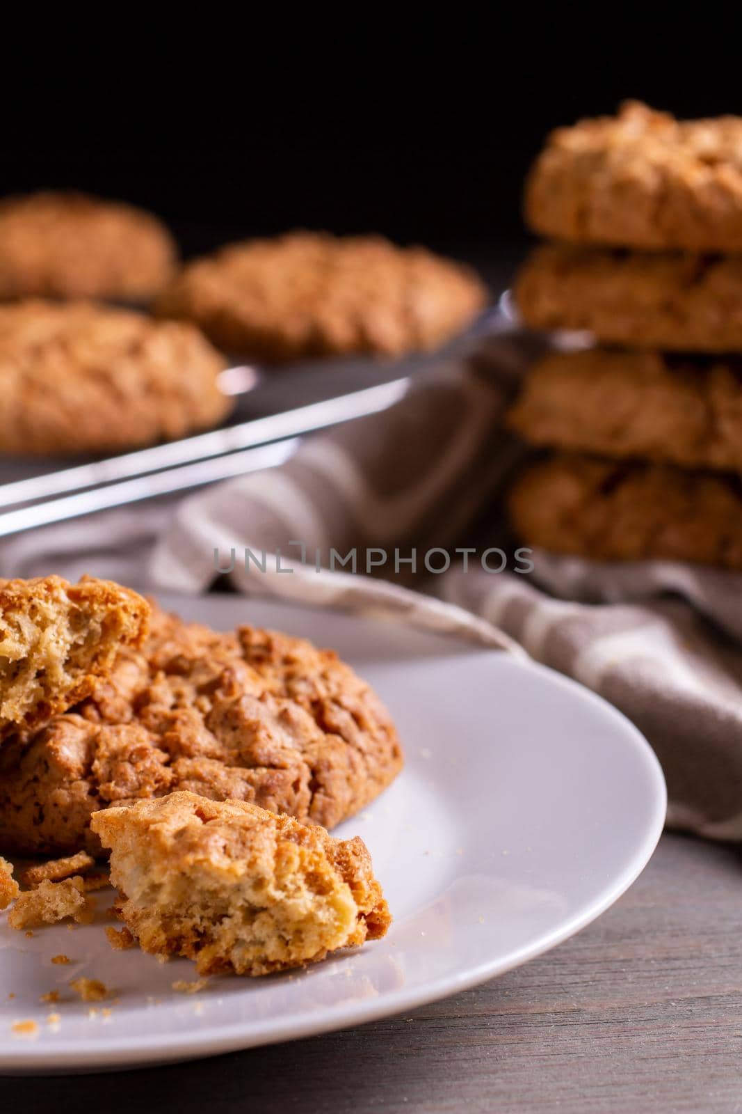 Freshly baked warm oatmeal cookies with towel on cooling rack on dark background