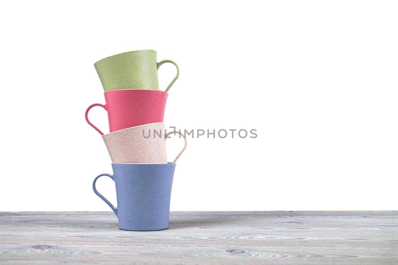 A stack of four ecological mugs on a wooden table on a white background. Dishes made of eco-plastic.