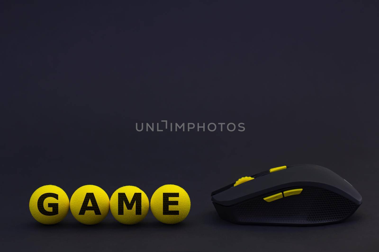 a black wireless computer mouse with yellow buttons on a background of a black grid textured in the form of hexagons and yellow soft balls with the inscription game