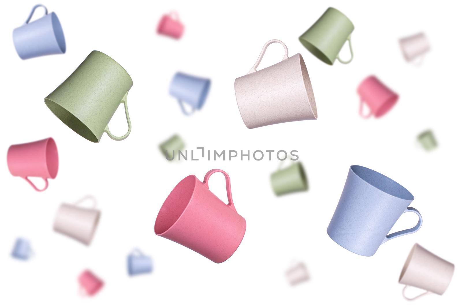 A lot of different colored plastic mugs flying in the air at different distances on a white background. Selected focus, background blur.