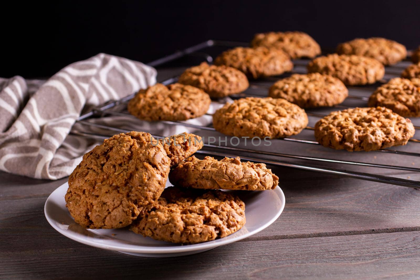 freshly baked warm oatmeal cookies on a cooling stand and saucer on a dark background.