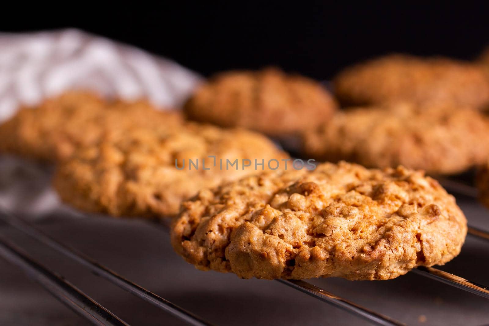 Freshly baked warm oatmeal cookies on a cooling rack on a dark background by bySergPo