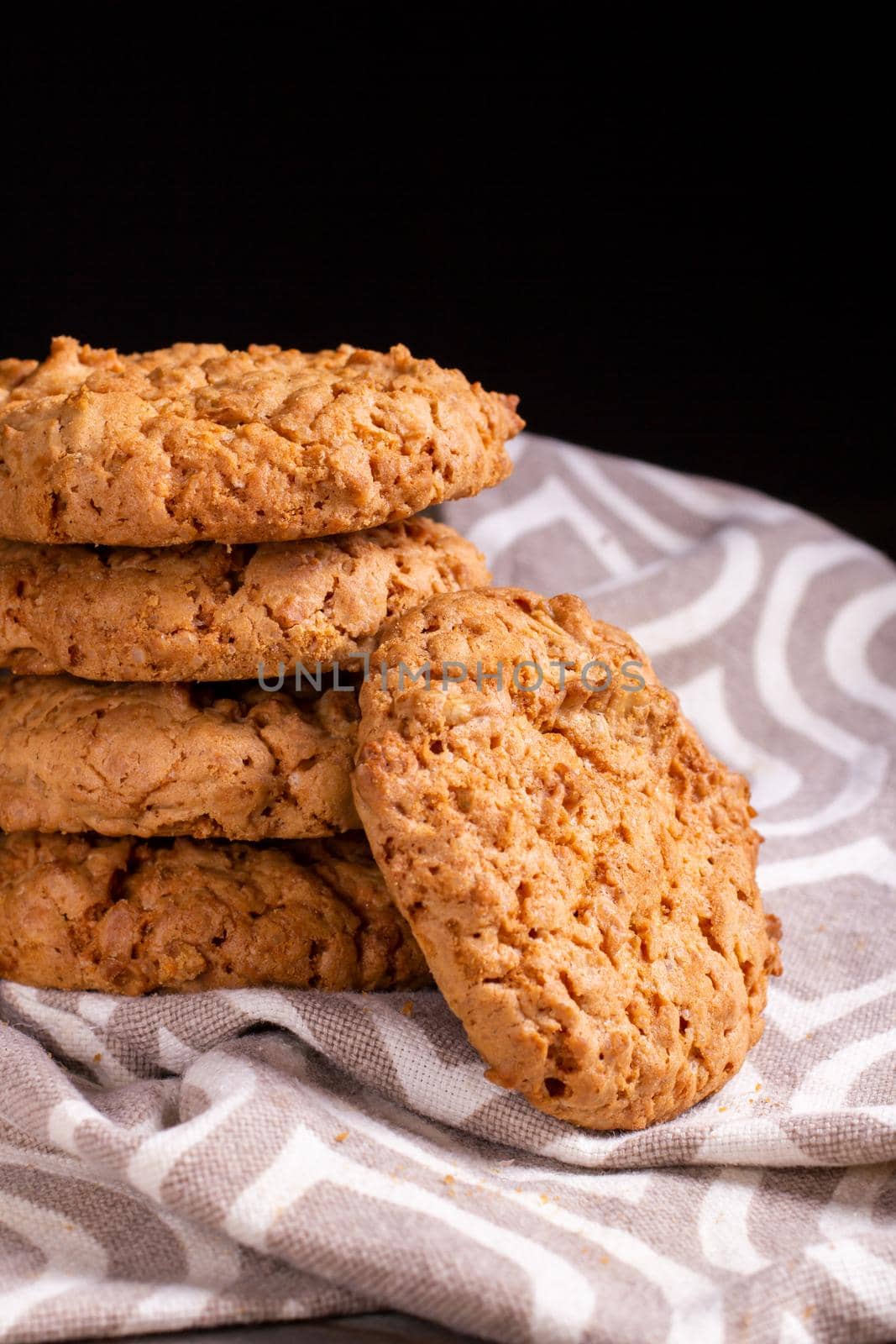 A stack of oatmeal cookies on a kitchen napkin on a wooden table against the dark background of the wal.