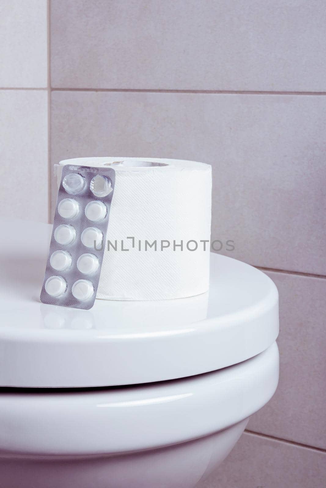 a roll of toilet paper with white pills on the toilet. vertical image.