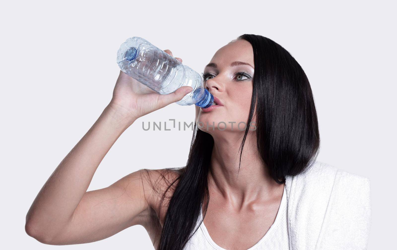 Athletic woman with towel on the shoulders drinks water from the bottle, isolated on white