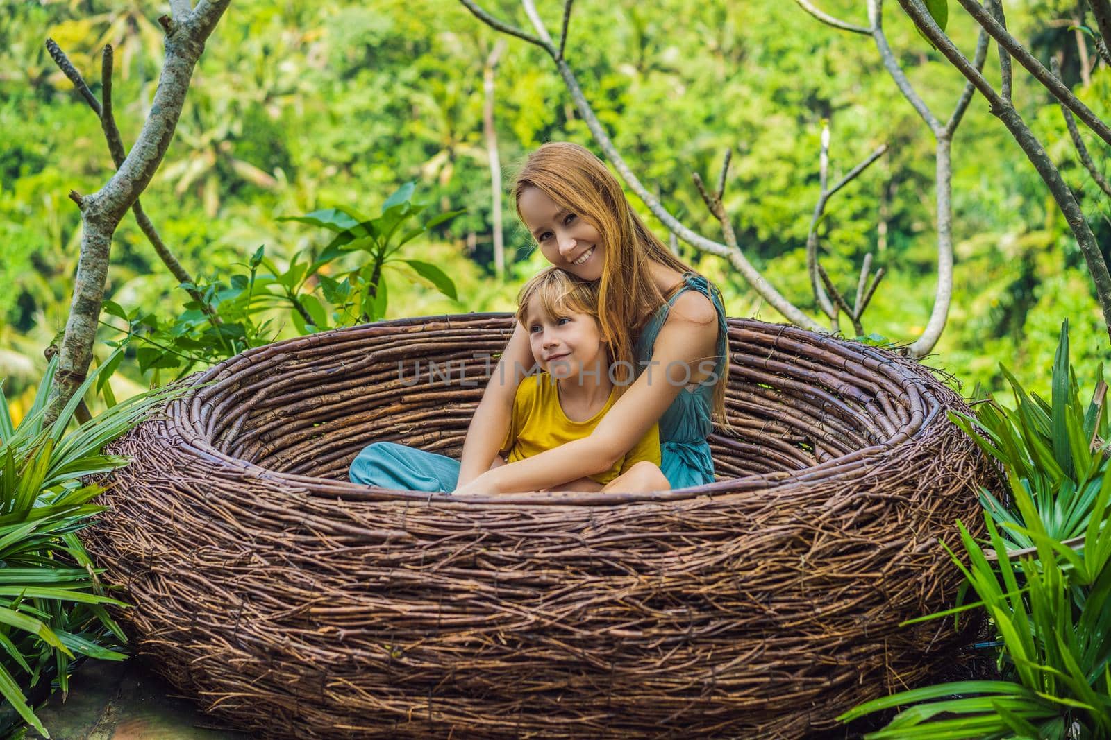 Bali trend, straw nests everywhere. Happy family enjoying their travel around Bali island, Indonesia. Making a stop on a beautiful hill. Photo in a straw nest, natural environment. Lifestyle. Traveling with kids concept. What to do with children. Child friendly place.