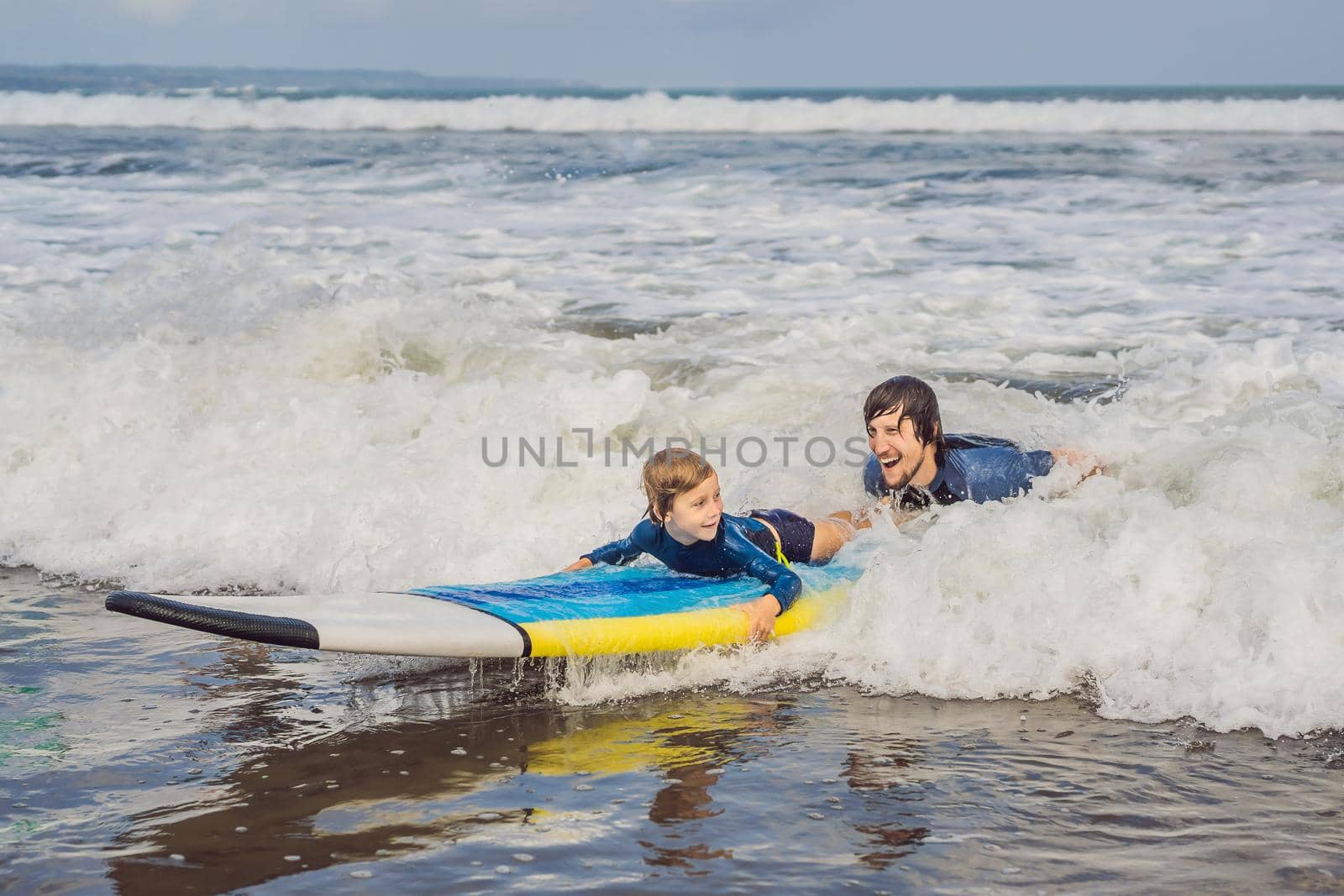 Father or instructor teaching his 5 year old son how to surf in the sea on vacation or holiday. Travel and sports with children concept. Surfing lesson for kids.