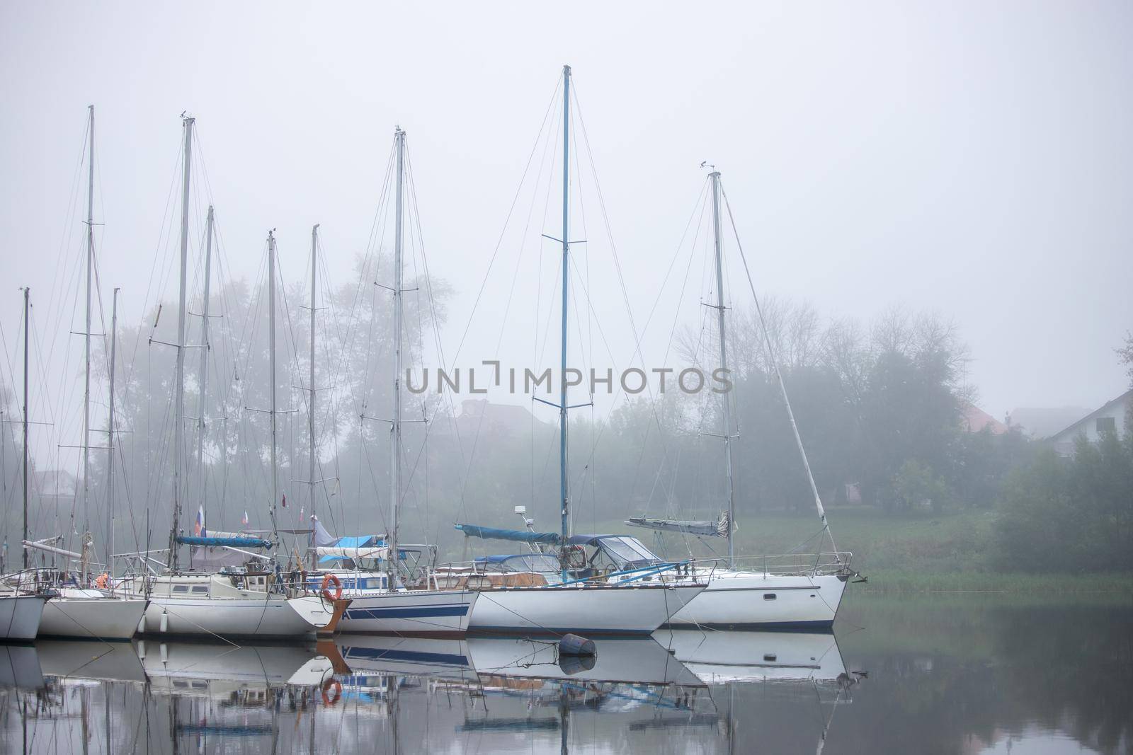 Yachts are small vessels moored to a pier in a thick fog. Sights, old harbor. by bySergPo