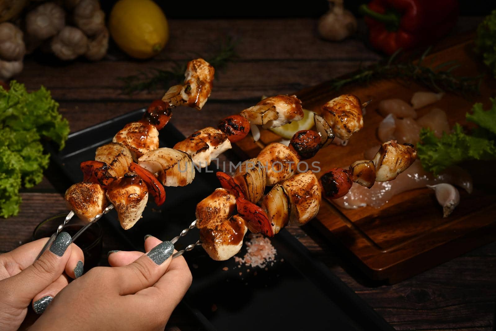 Close up vie woman hand holding delicious barbecue skewers with grilled chicken, cherry tomato, sweet pepper and onions.