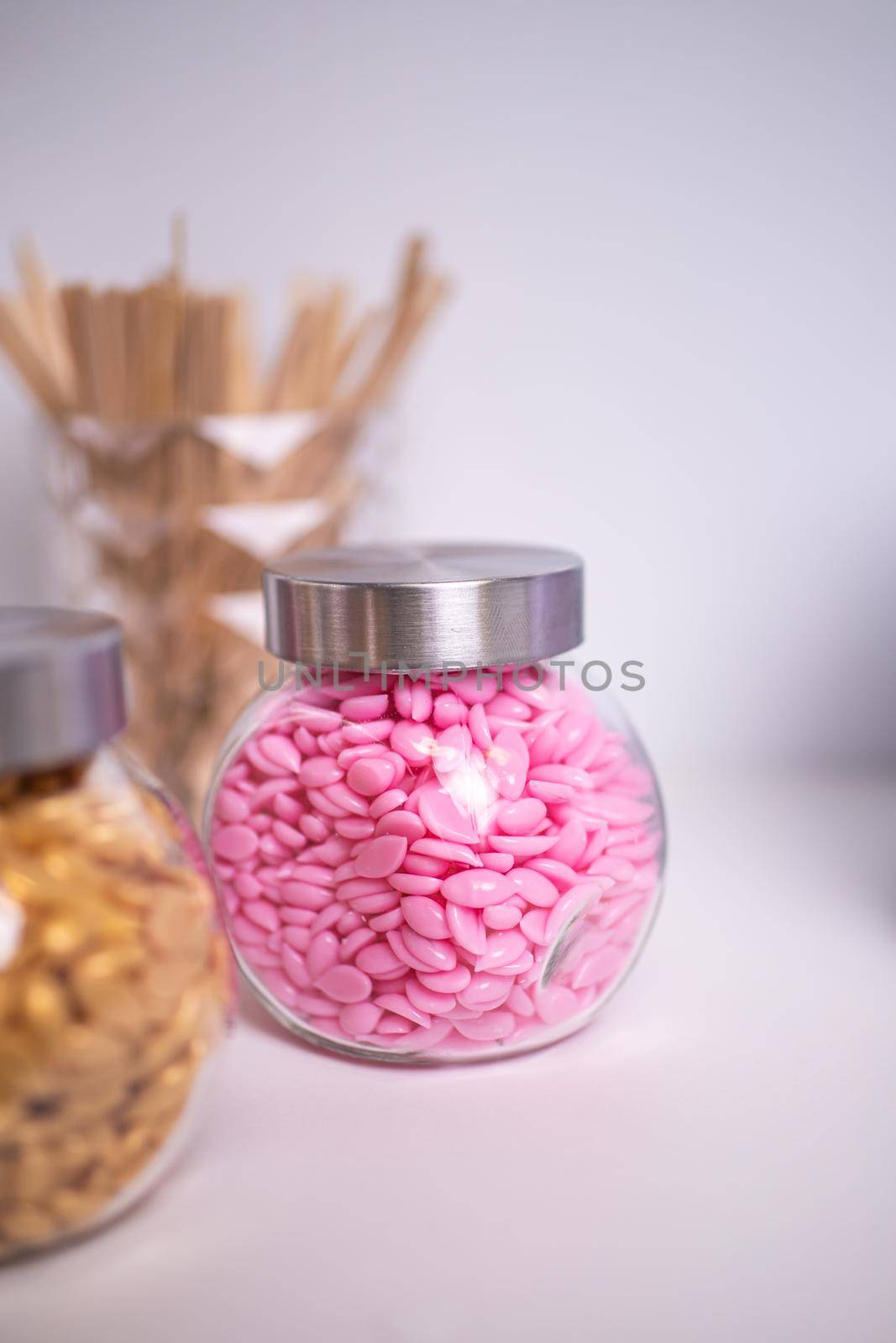 Glass jars filled with wax granules for depilation with wooden blades on a blurred background. selected focus