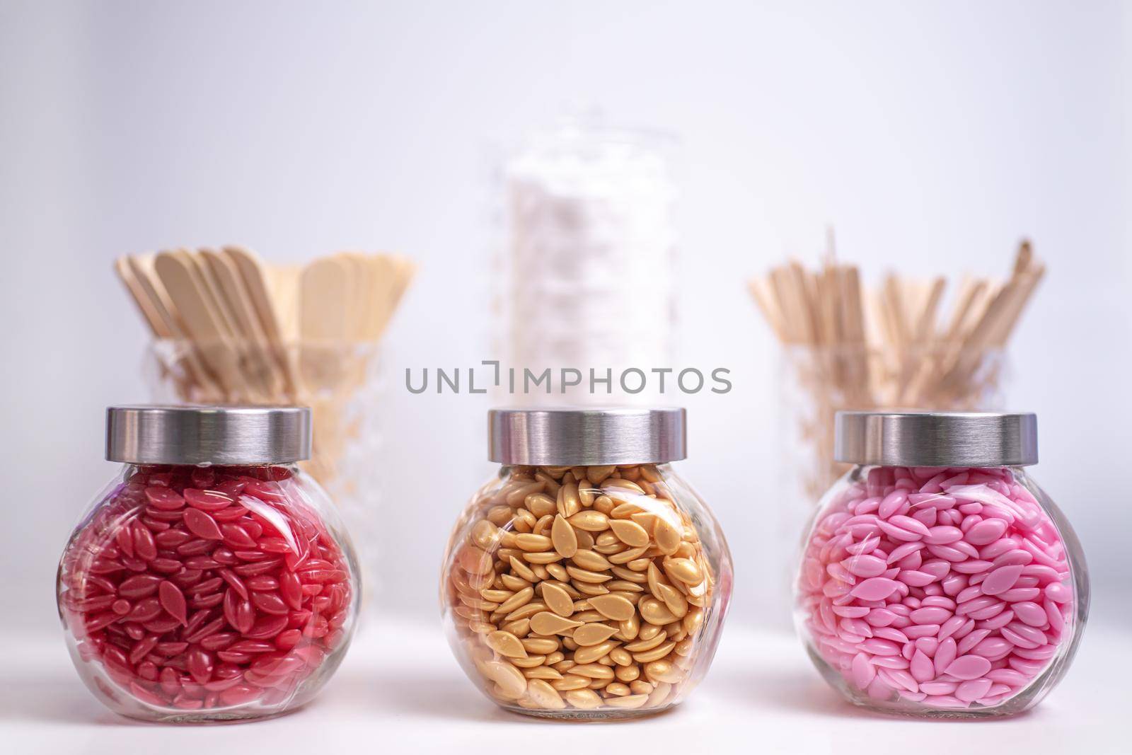 Glass jars filled with wax granules for depilation with wooden blades on a blurred background. selected focus