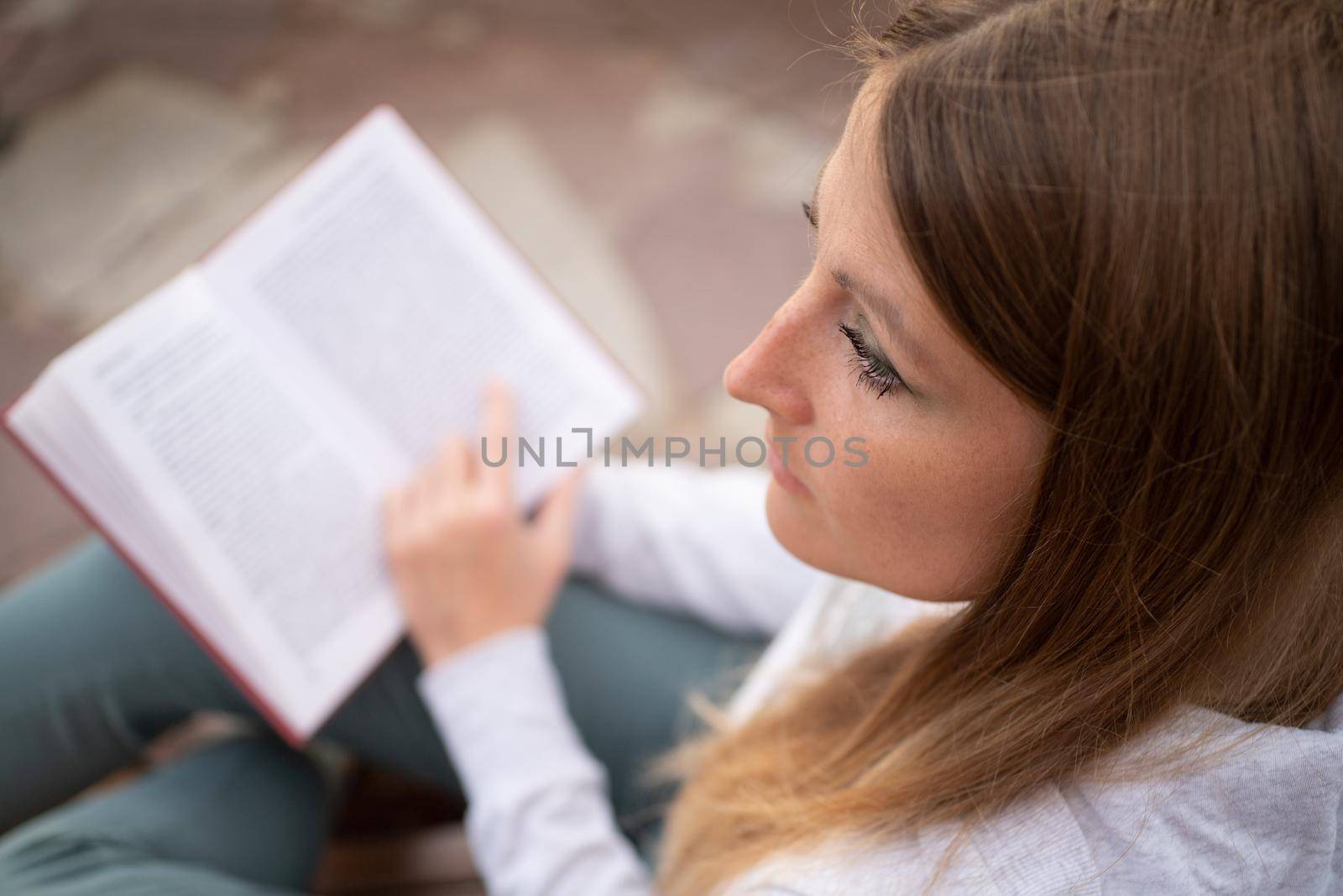 Top view of a woman reading a book. A young woman looks away distractedly with a book in her hands. by bySergPo