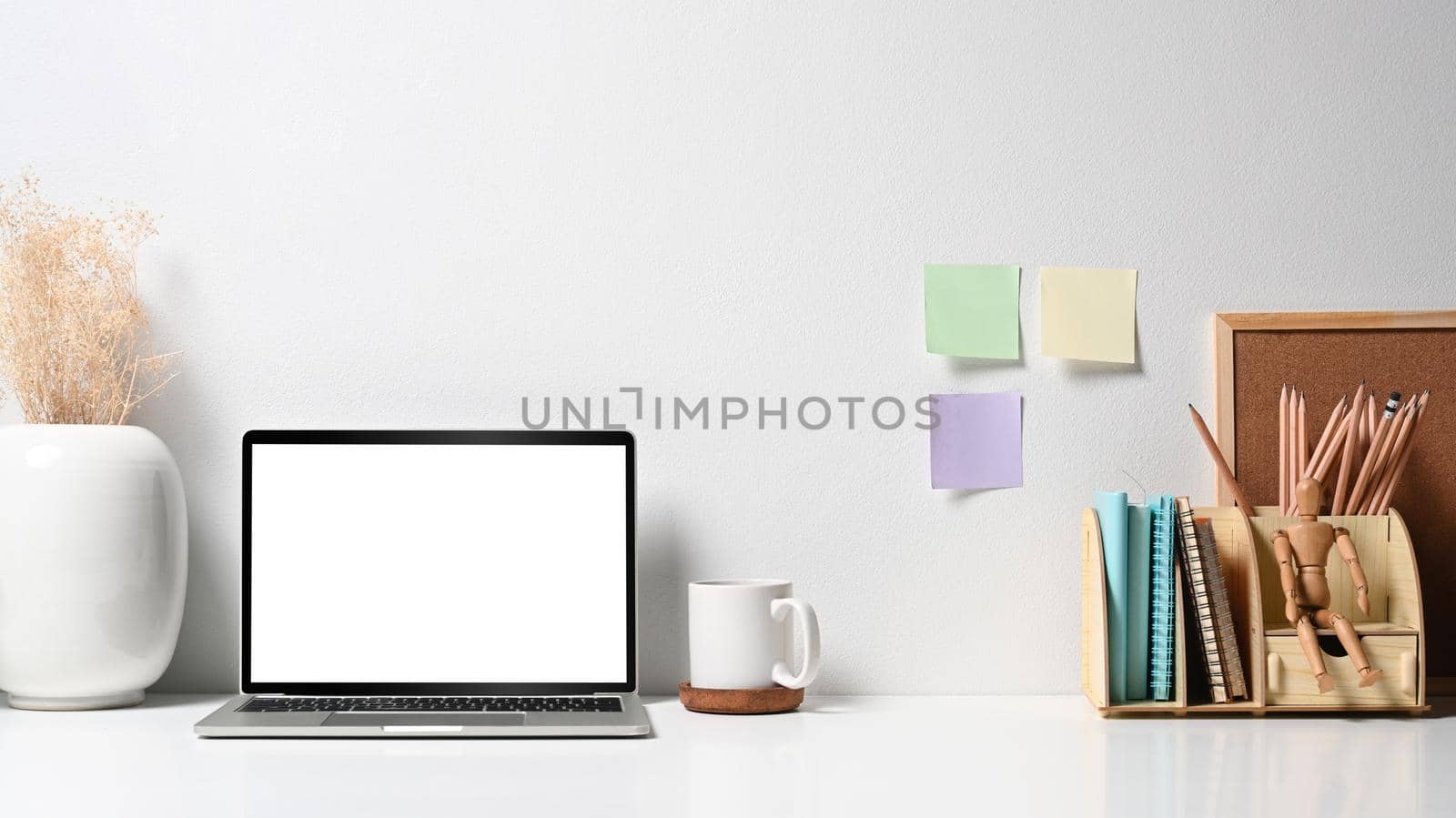 Mockup laptop computer with blank screen, flower pot, coffee cup and stationery on white table. Home office desk.