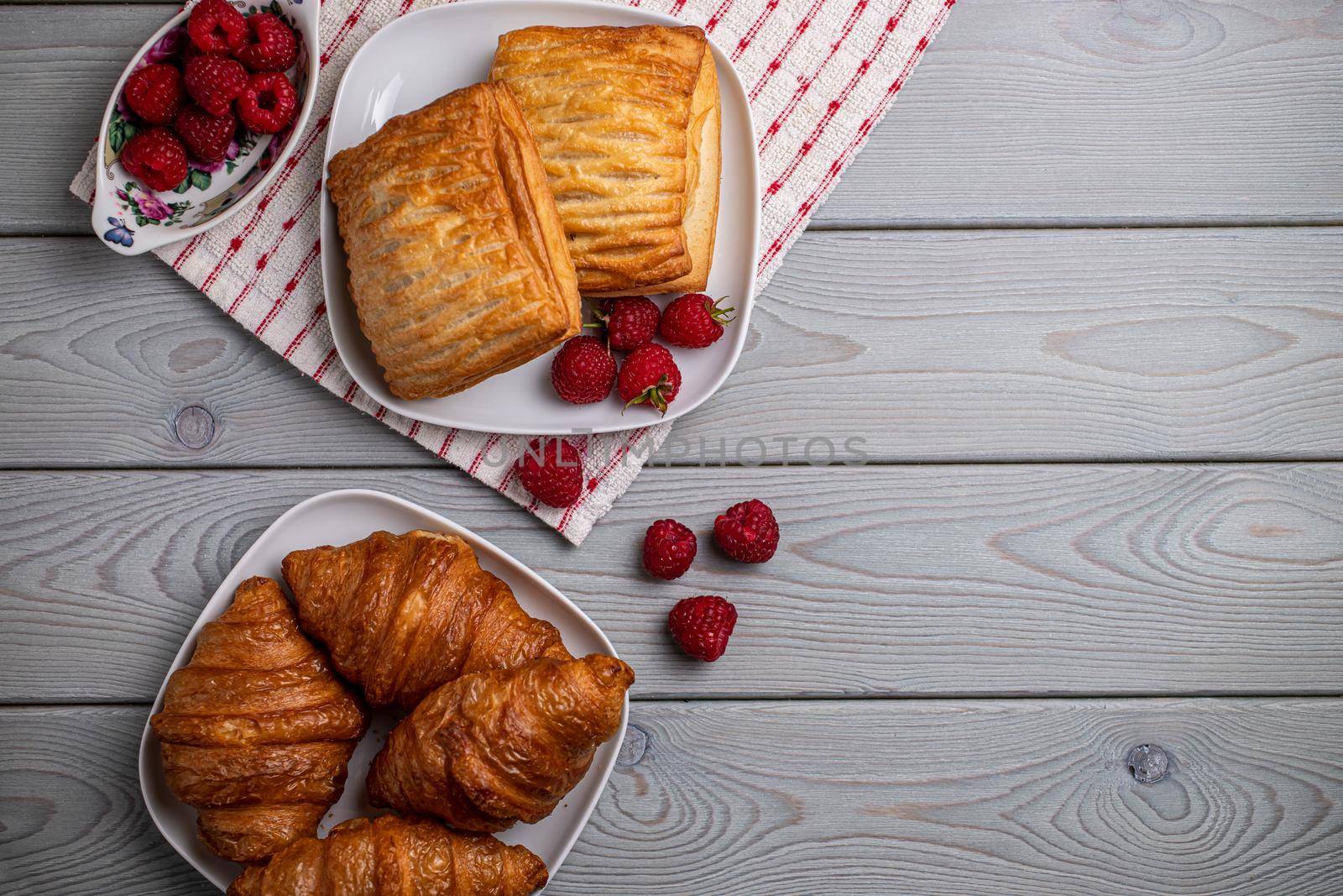 Delicious fresh croissants and sweet raspberry puffs on a wooden table.