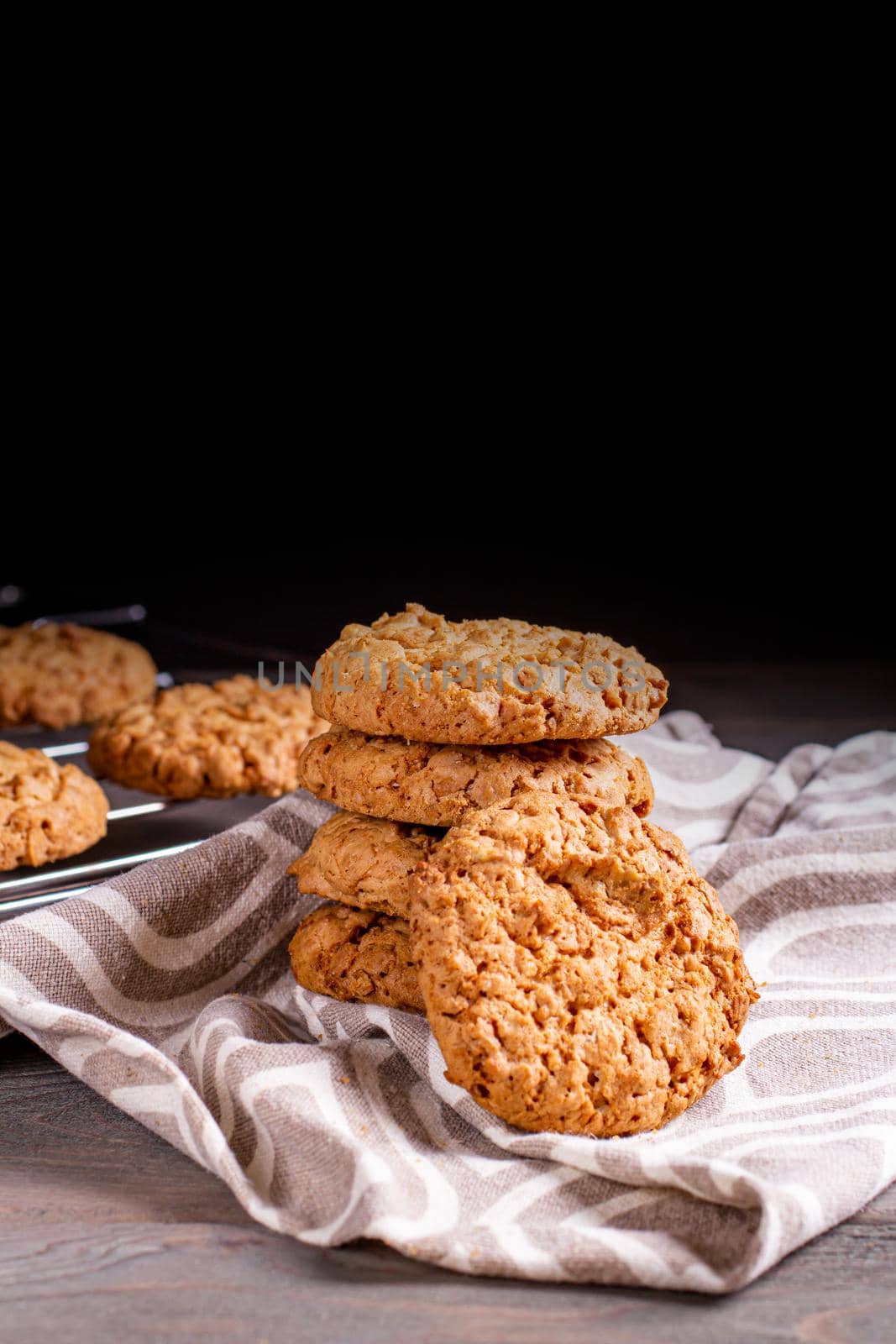 A stack of oatmeal cookies in a saucer and a napkin on a wooden table on a dark background.