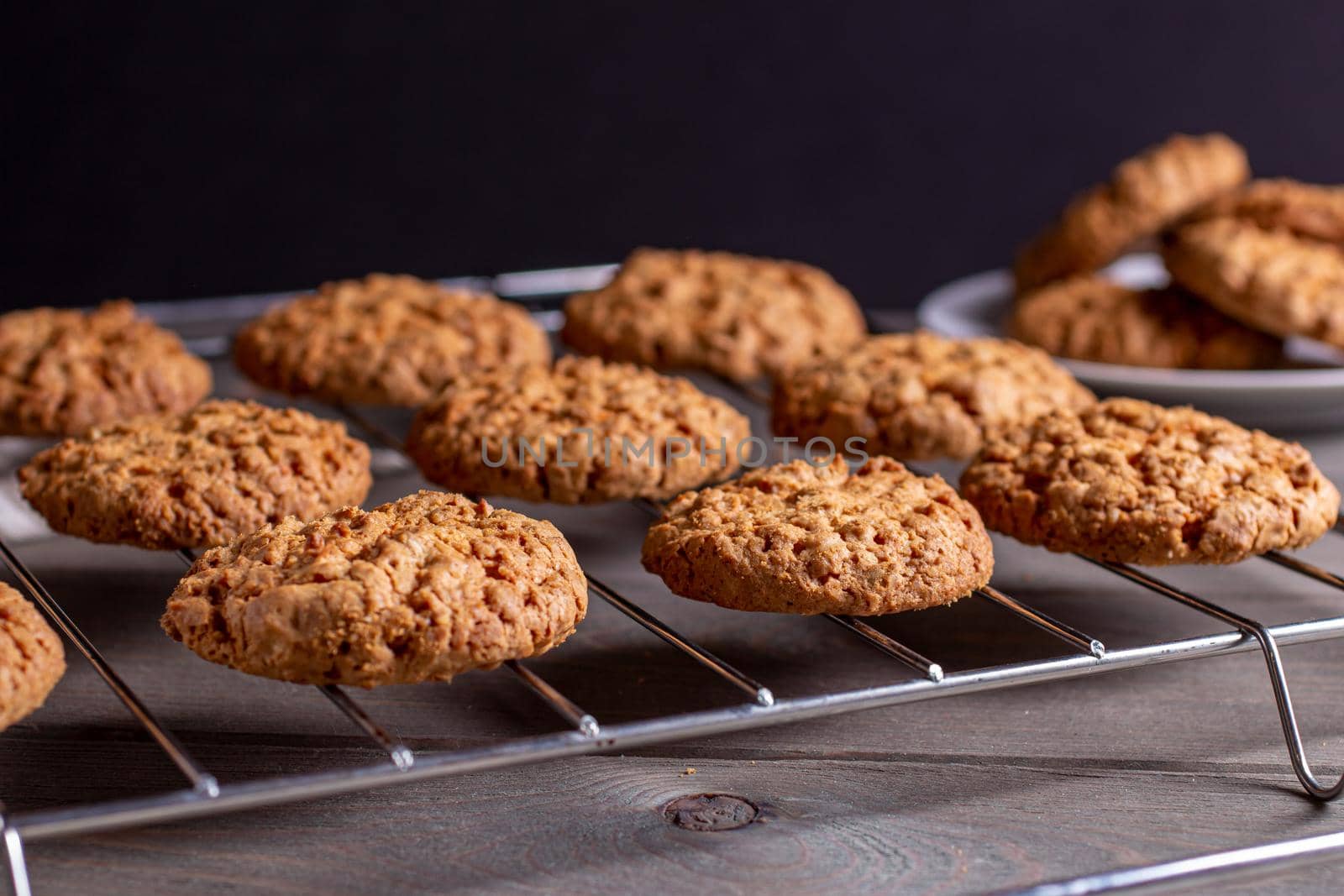 Close-up of a freshly baked stack of warm oatmeal cookies on a cooling rack and saucer on a dark background. the view from the side