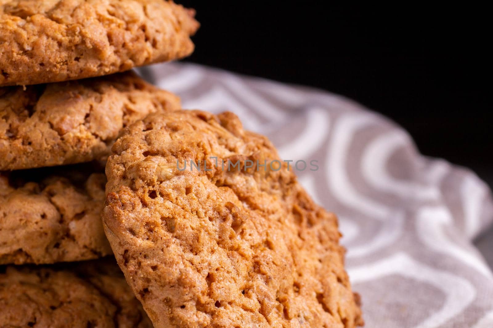 A stack of oatmeal cookies on a kitchen napkin on a wooden table against the dark background by bySergPo