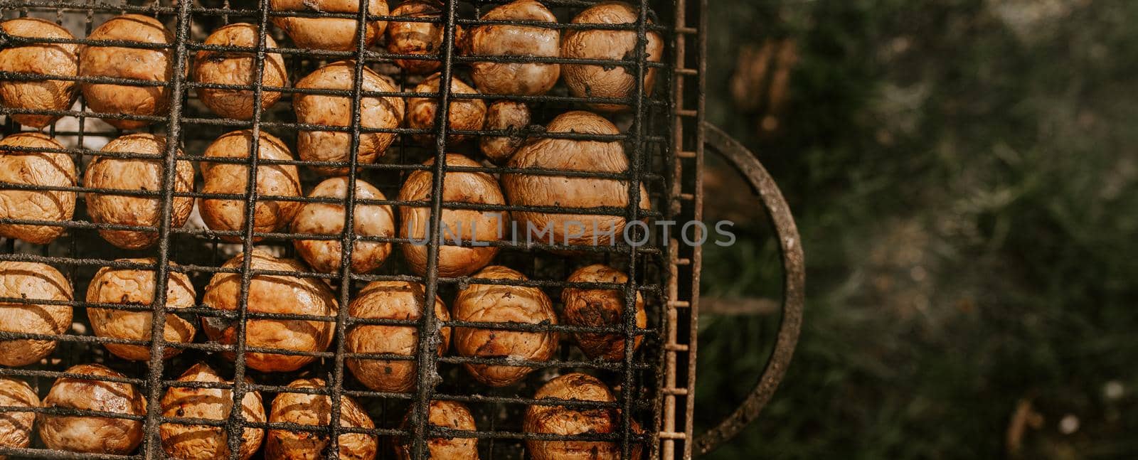 white identical small round mushrooms champignons stacked in even rows in a barbecue on the grill. Green grass background. Summer. White smoke over baked vegetables.