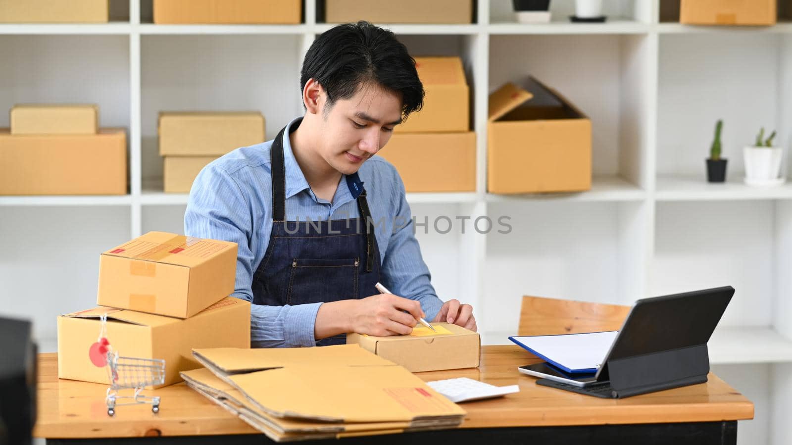 Young man online seller prepare parcel box of product for deliver to customer. Concept of online selling, e-commerce.