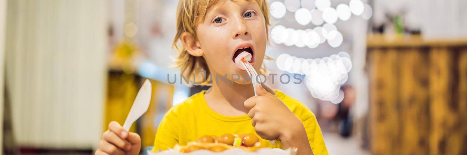 A little boy eats dessert waffles with jam in a cafe. BANNER, LONG FORMAT
