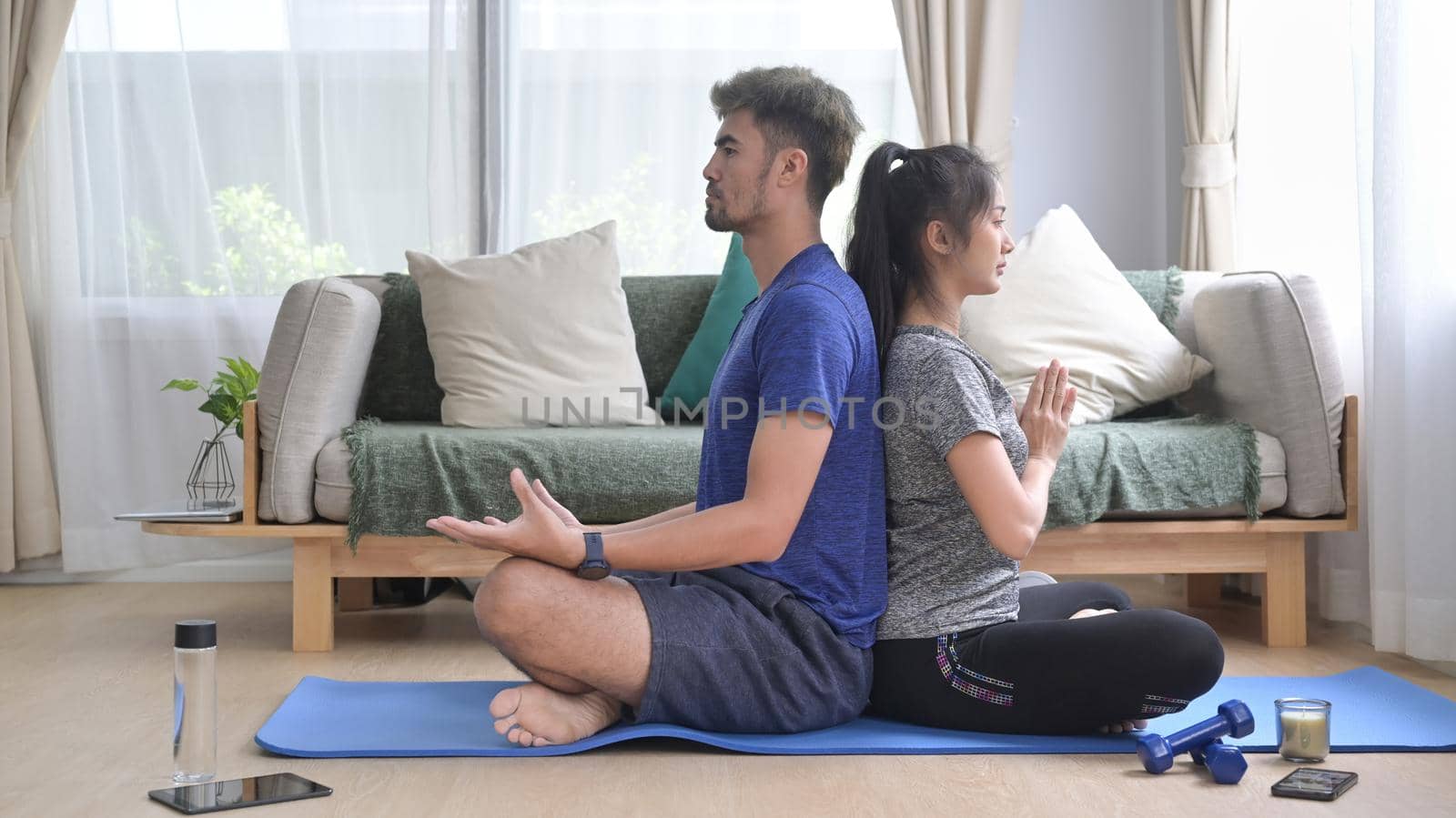 Healthy young couple meditating, sitting in lotus position on mat. Healthy lifestyle, yoga, pilates, exercising concept.