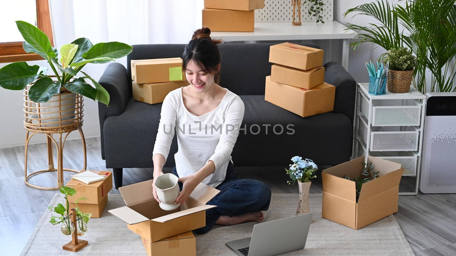 Happy young business woman small business owner packing product in cardboard box for delivery to customers. Online selling, e-commerce concept.