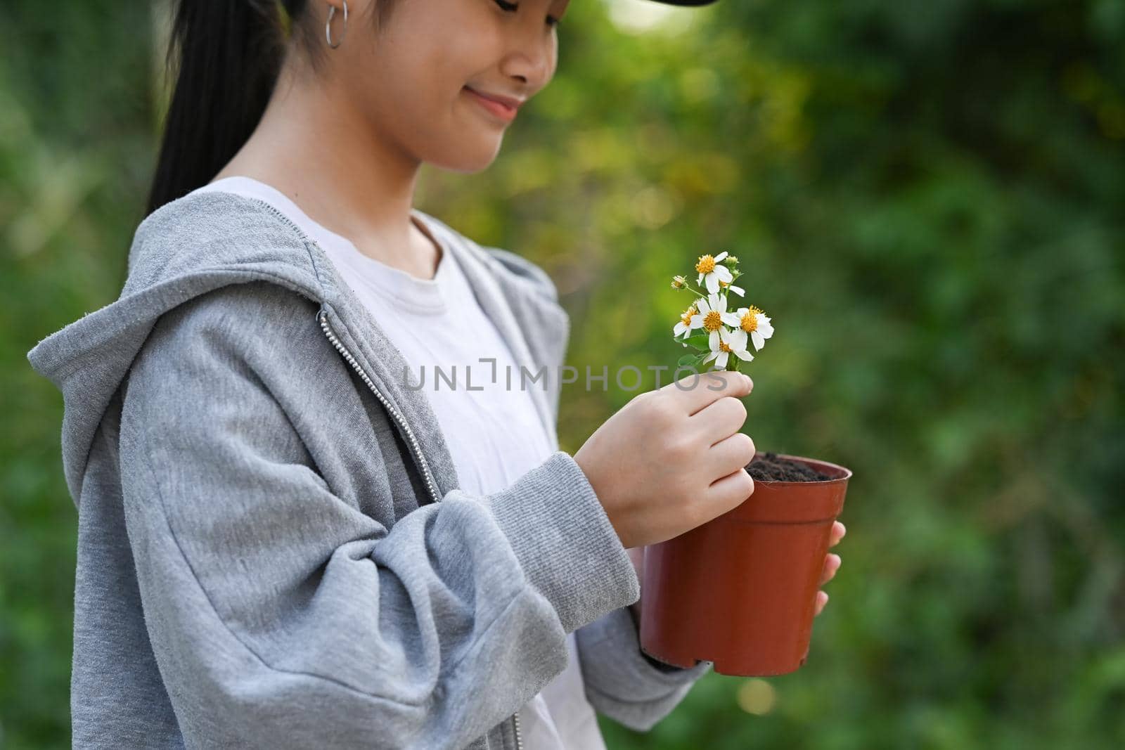 Cute asian girl holding potted plant in hands against blurred green nature background. Earth day, Ecology concept.