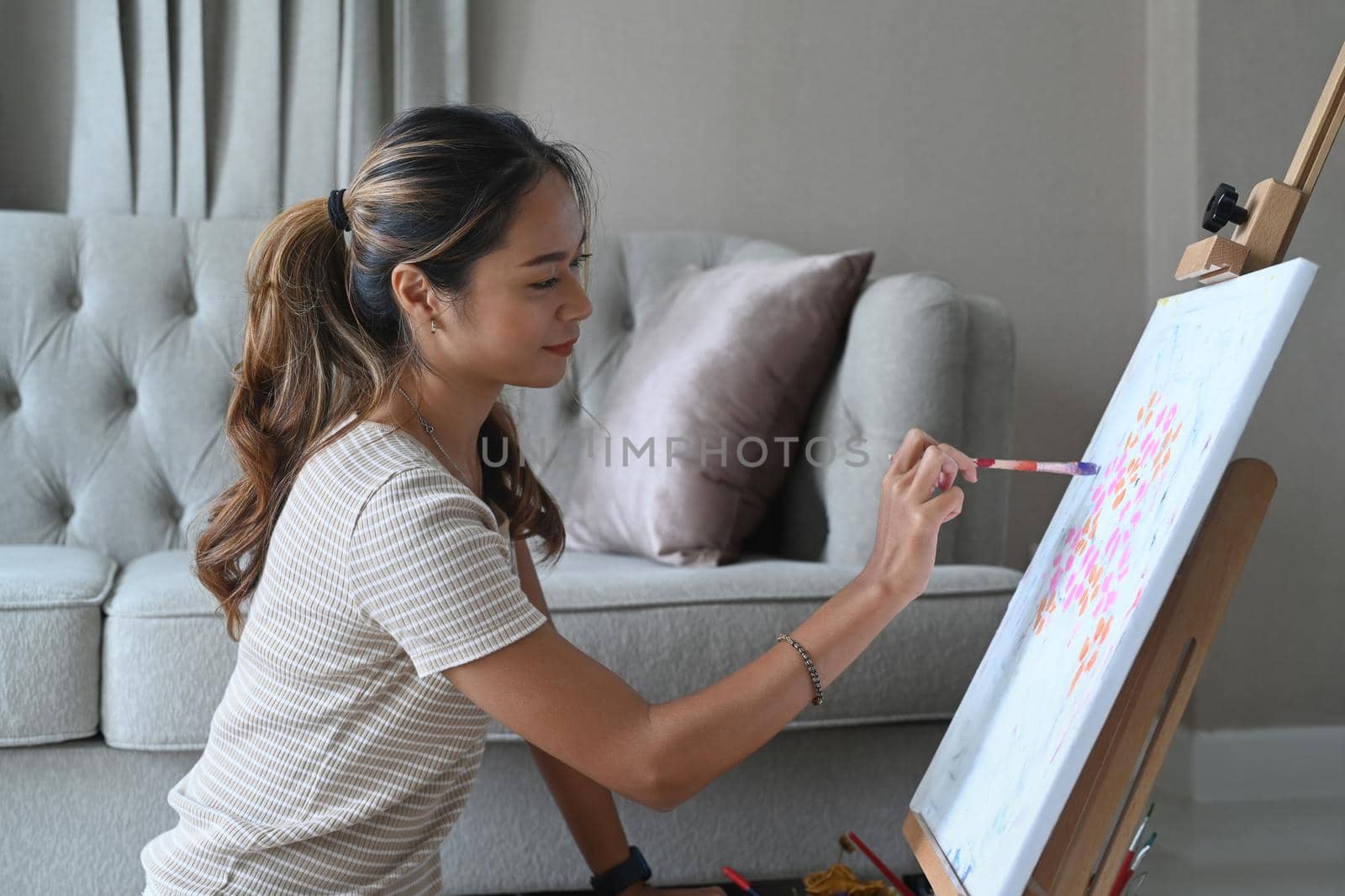 Peaceful young woman painting picture on canvas with watercolor.