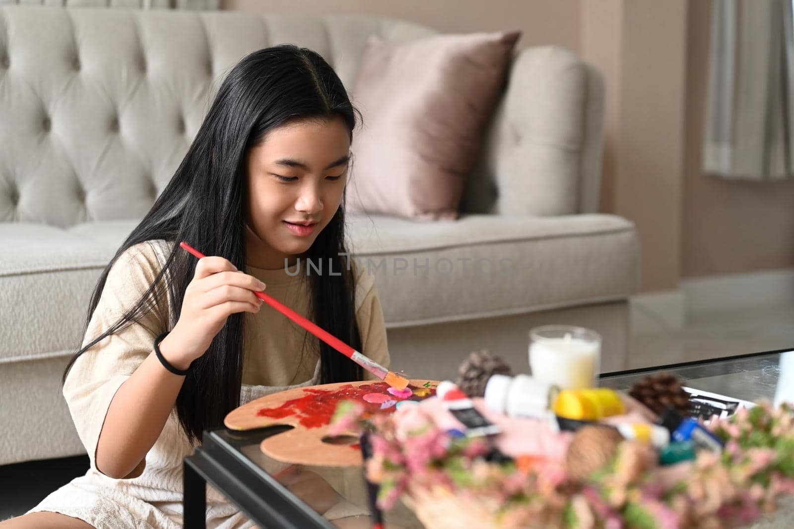 Elementary girl spending leisure time at home and painting with watercolors.