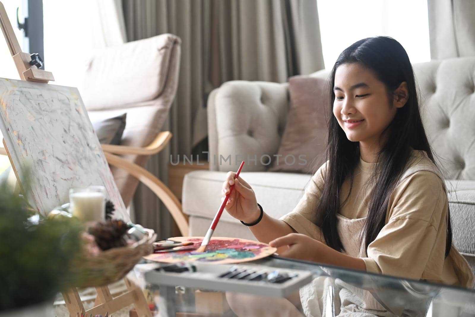 Cute girl enjoy painting picture with watercolors while spending leisure time at home.