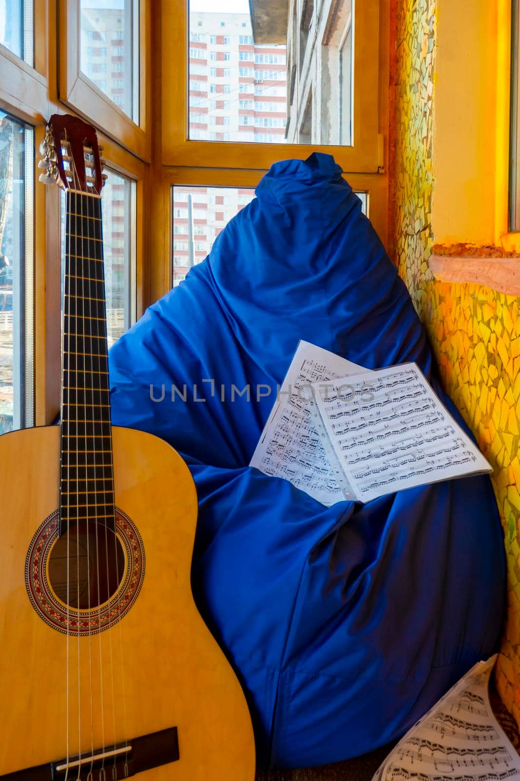 A glazed golden-orange balcony in a winter city, a place to relax with a blue paint bag, guitar and sheet music. The concept of music, relaxation and hobbies