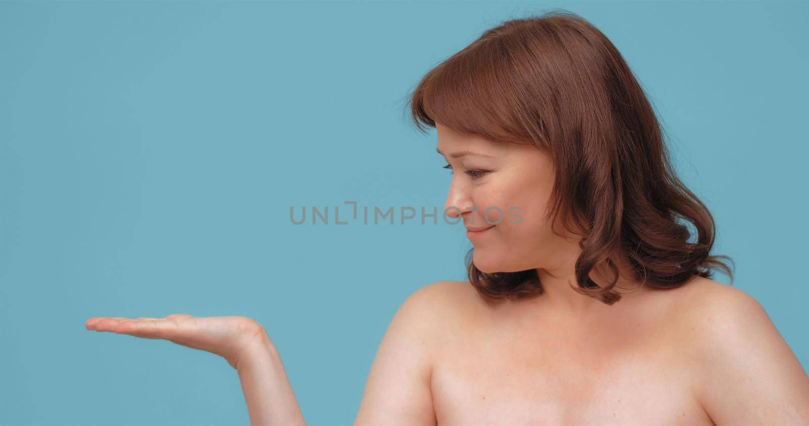 Cheerful mature woman holding open hand for embedding skin care visualization. Smiling woman advertise anti-age cream isolated on color background.