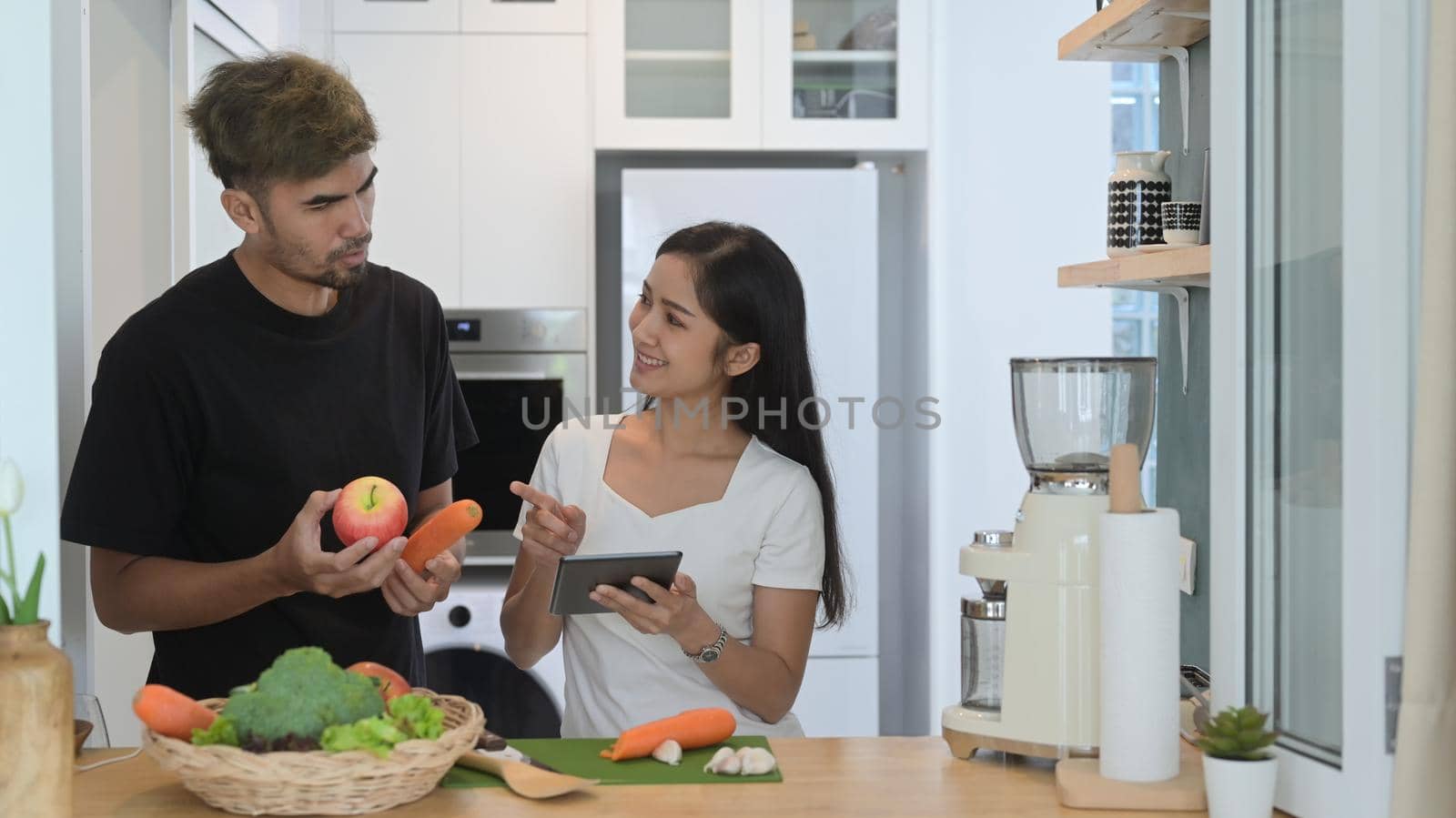 Happy young couple preparing ingredient for making making green detox smoothie in home kitchen.