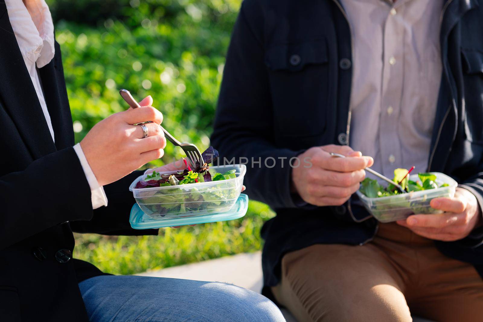 detail of the hands of two people eating a salad in a park during a work break, concept of healthy fast food at work