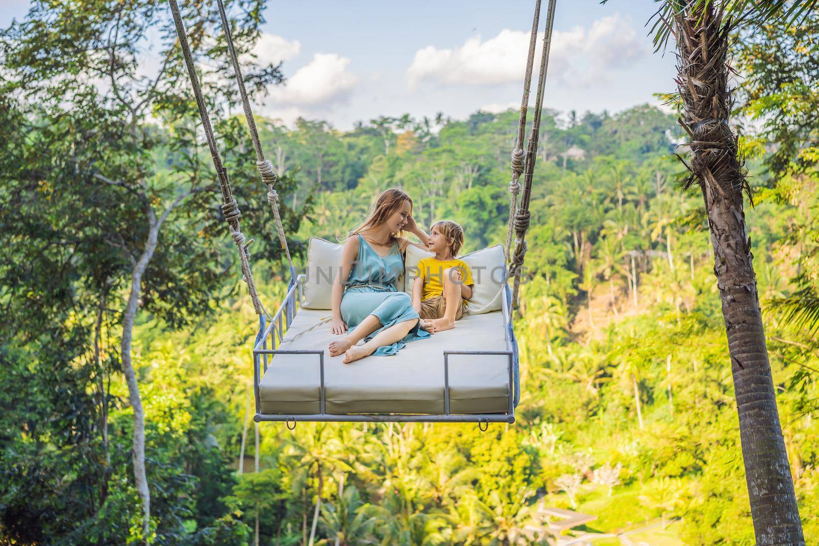 Mother and son swinging in the jungle rainforest of Bali island, Indonesia. Swing in the tropics. Swings - trend of Bali. Traveling with kids concept. What to do with children. Child friendly place by galitskaya