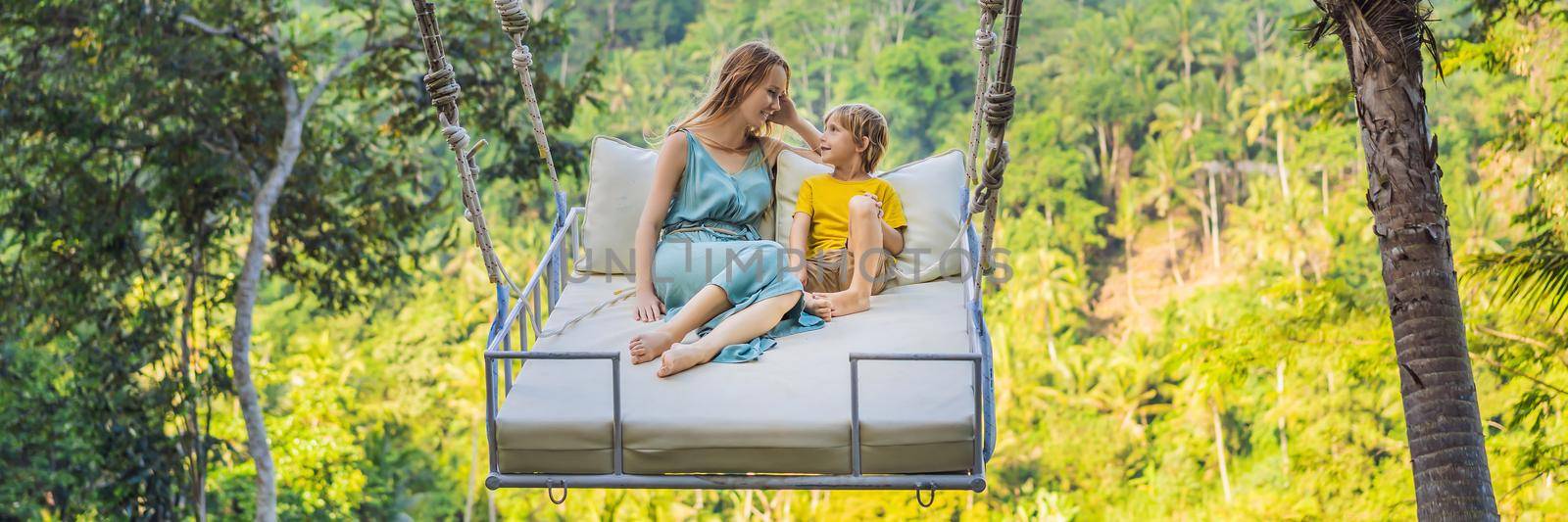 BANNER, LONG FORMAT Mother and son swinging in the jungle rainforest of Bali island, Indonesia. Swing in the tropics. Swings - trend of Bali. Traveling with kids concept. What to do with children. Child friendly place by galitskaya